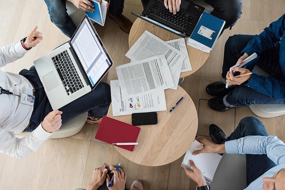 An overhead view of a group of people brainstorming around a couple of tables and laptops